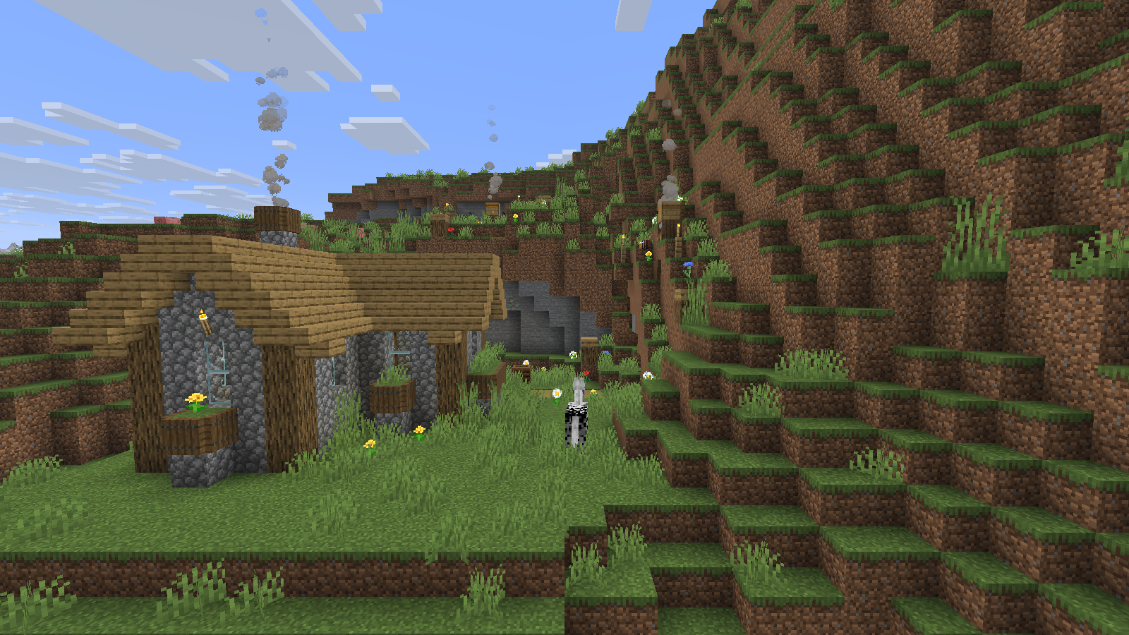 The farmstead has a pale wooden roof and flower boxes; smoke rises near beehives higher on the grassy slope.