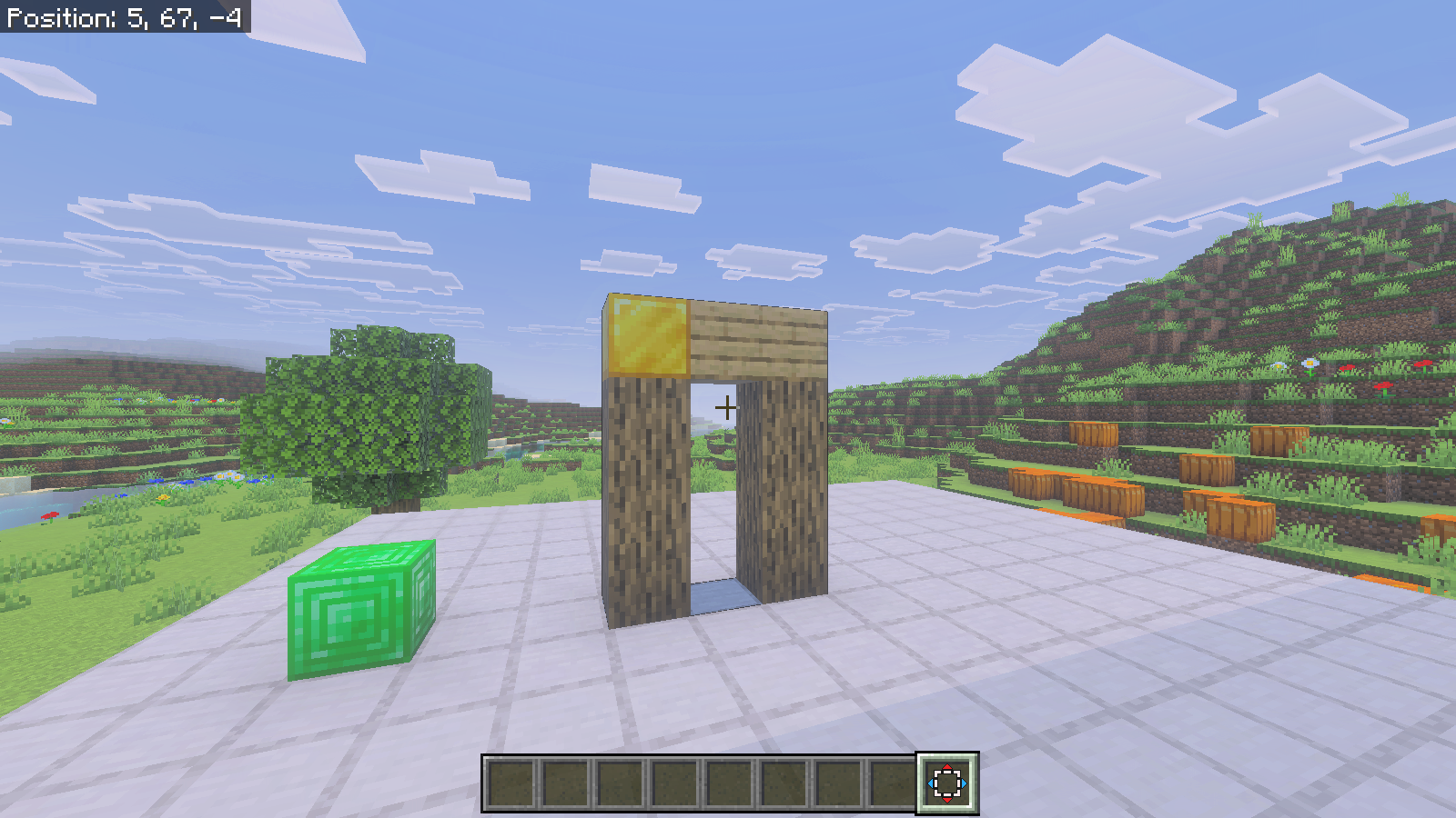 An oak-log arch with a gold corner stands beside a separate emerald block on the platform; the Nudge tool is selected.