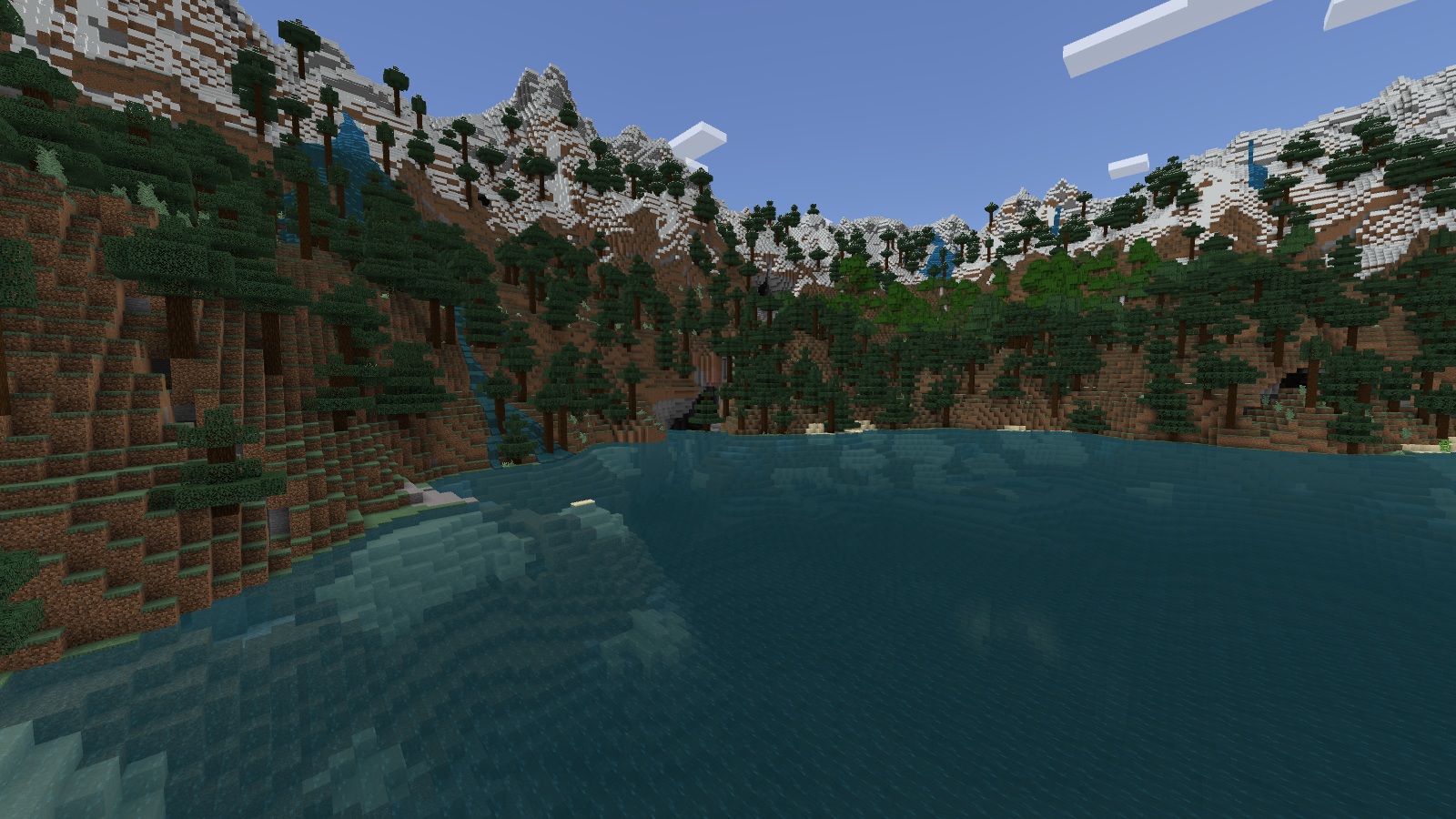 View across a Bedrock lake toward steep spruce-covered banks, waterfalls and snowy mountain ridges.