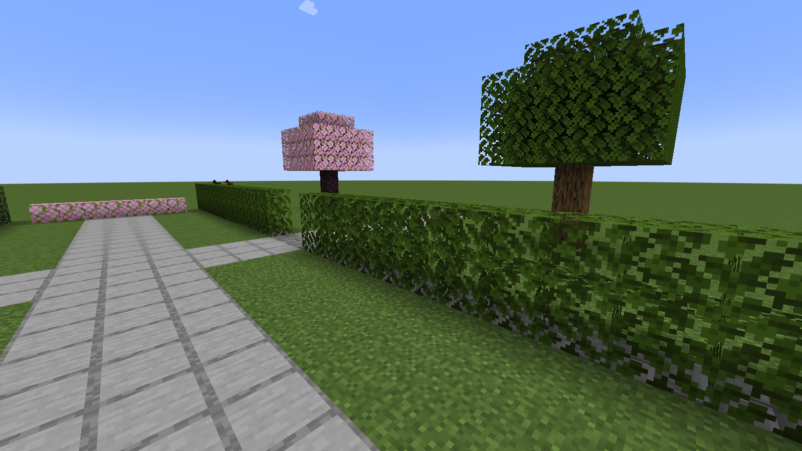 Default oak leaves form a straight two-block-high hedge beside a stone garden path.